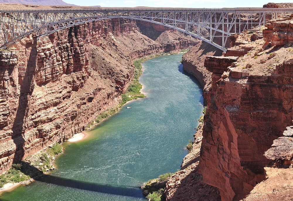 A steel arch highway bridge spanning a red-rock canyon above a river in Arizona