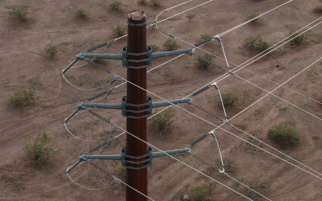 Top of a steel transmission pole with insulators and conductors seen from a drone